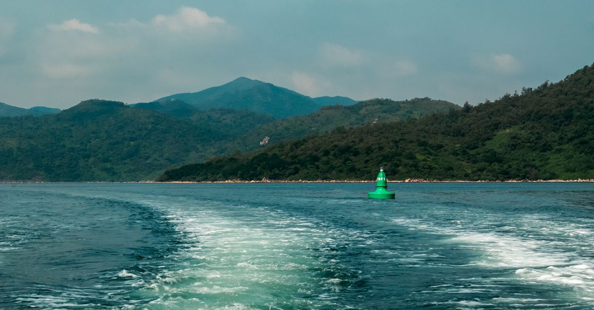 A tranquil lake scene featuring a green buoy against a mountain backdrop on a clear day.