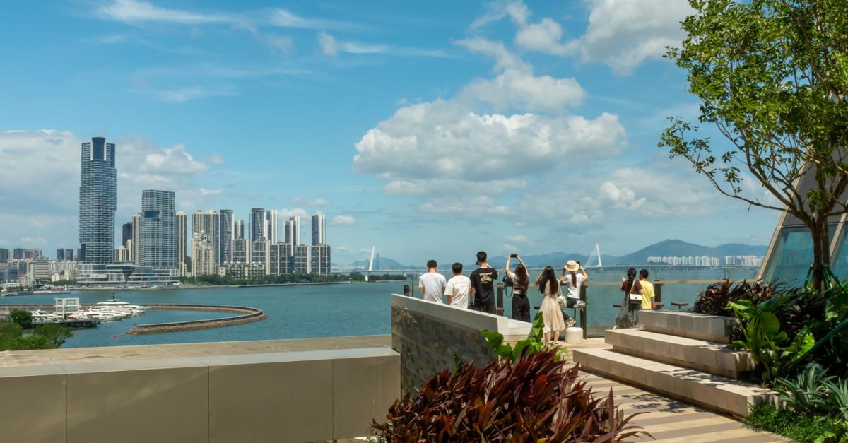 Scenic view of Shenzhen Bay with people enjoying the skyline from a green terrace.