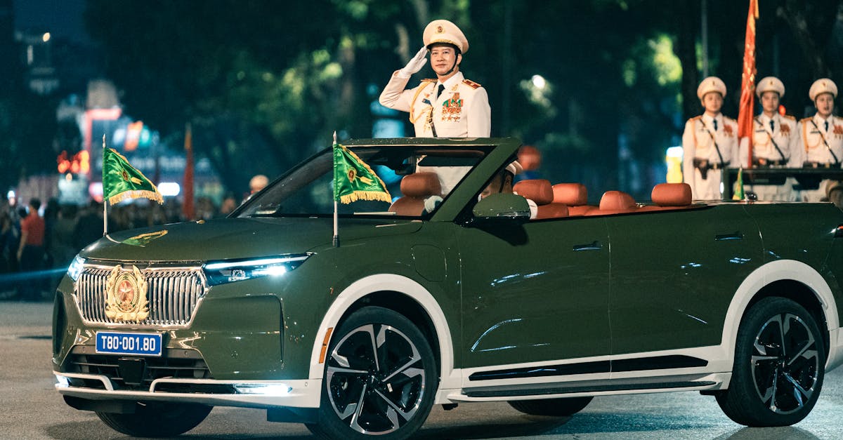 A military officer saluting during a parade in Hanoi with a convertible car and flags.