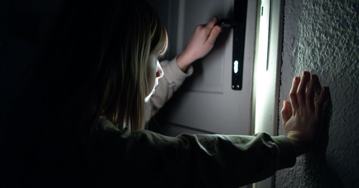 A child opening a door in dim light, casting shadows and a mysterious atmosphere.