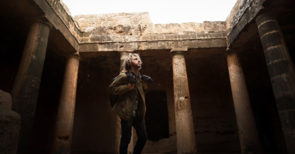 Man exploring ancient rock tombs with columns in Cyprus, highlighting historical architecture.