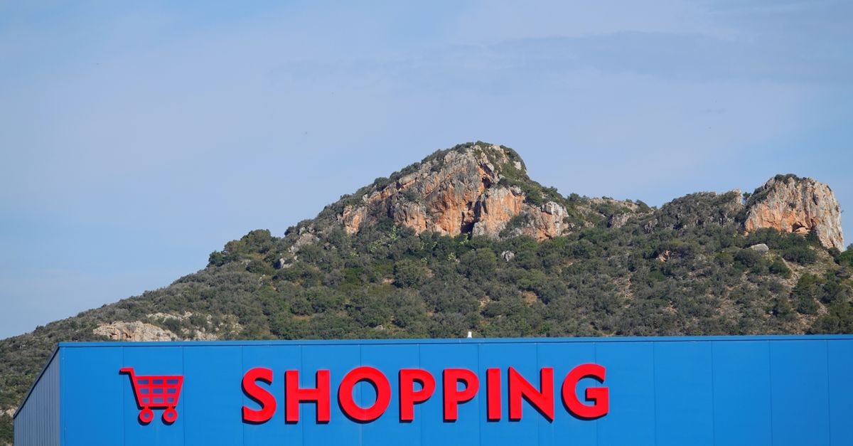 Shopping center sign with red text against a backdrop of a rocky mountain in Cala Millor.