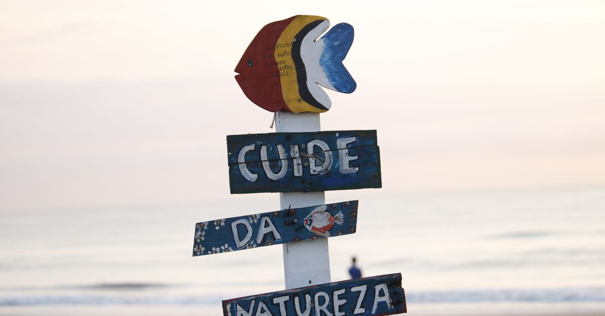 Colorful beach sign in Guaratuba, Brazil, promoting nature care at sunrise by the ocean.