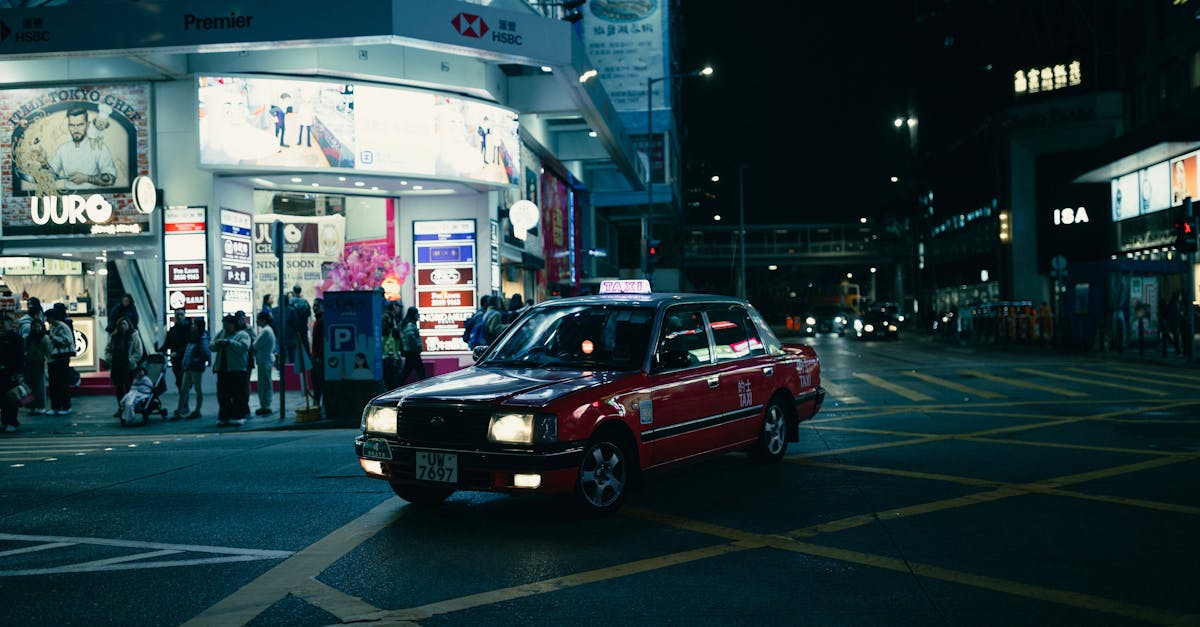 A classic red taxi navigates the bustling streets of Hong Kong at night under neon lights.