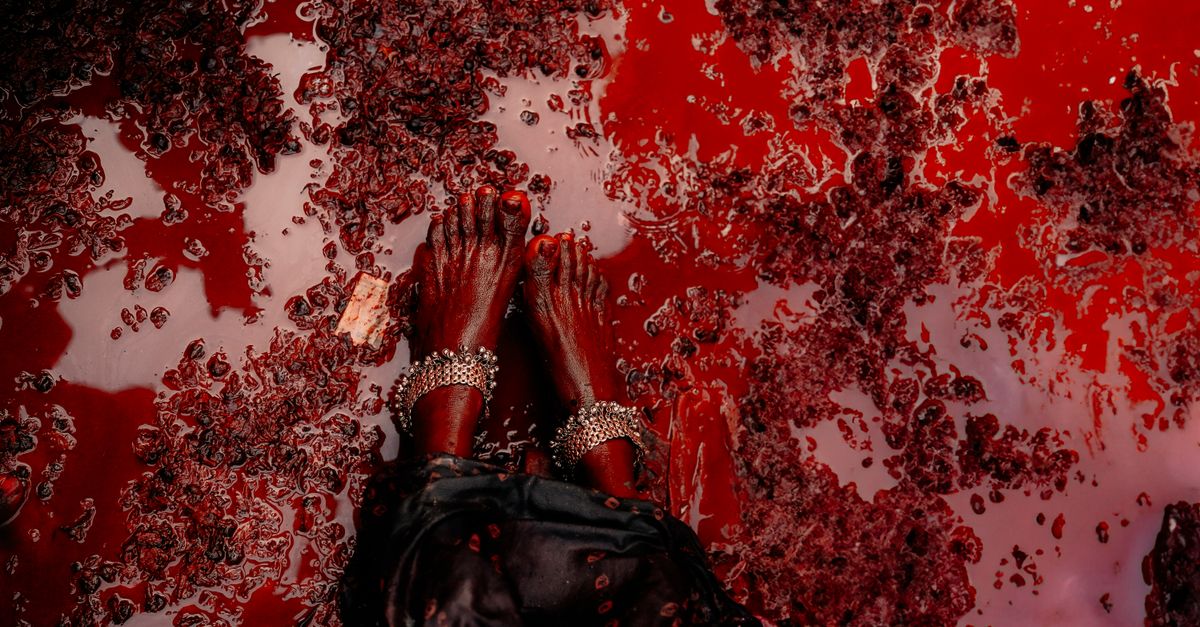 Artistic close-up of feet with anklets submerged in vivid red liquid.