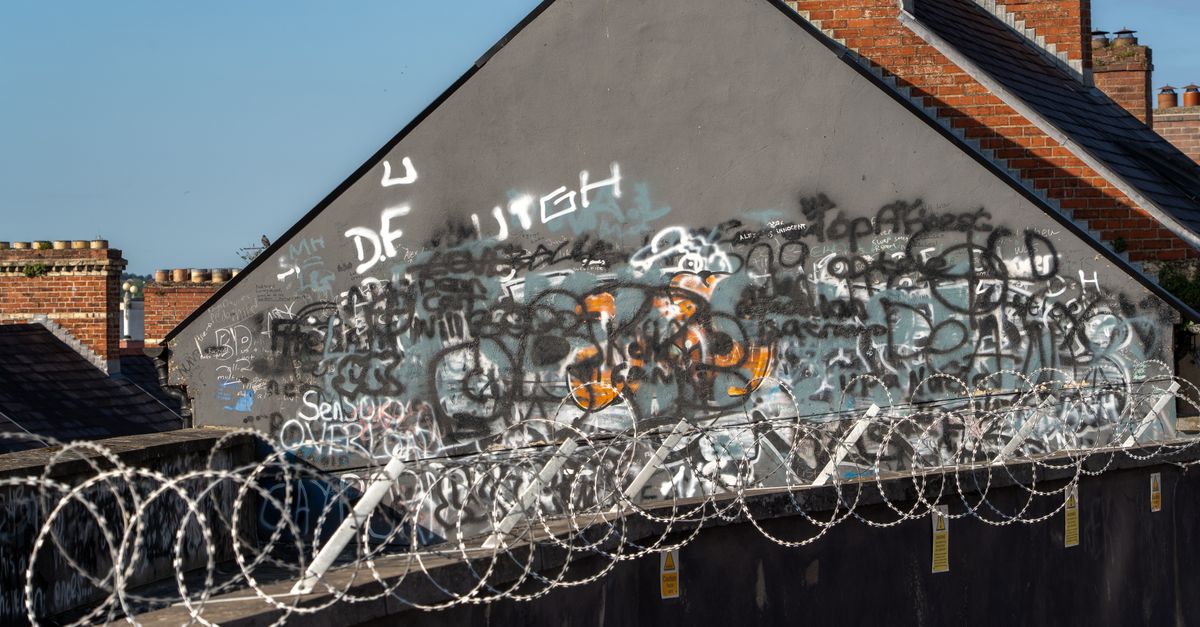 Graffiti on a wall with barbed wire in an Irish urban setting, showcasing street art and security measures.