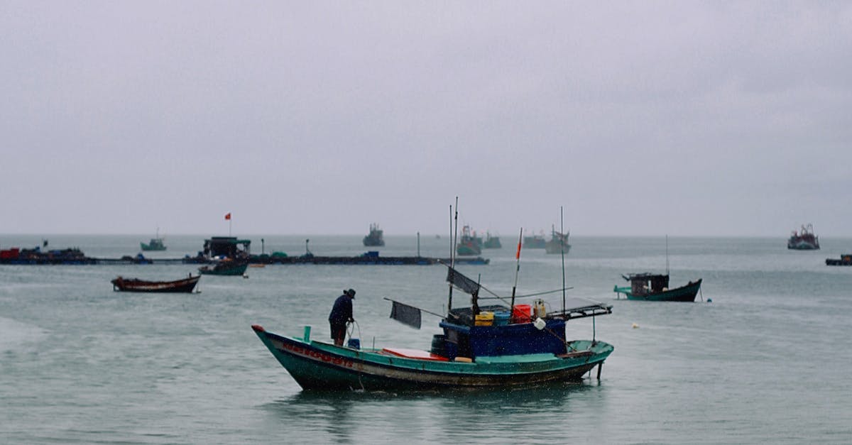 A fishing boat manned by a fisherman navigates through the cloudy sea, surrounded by other boats.