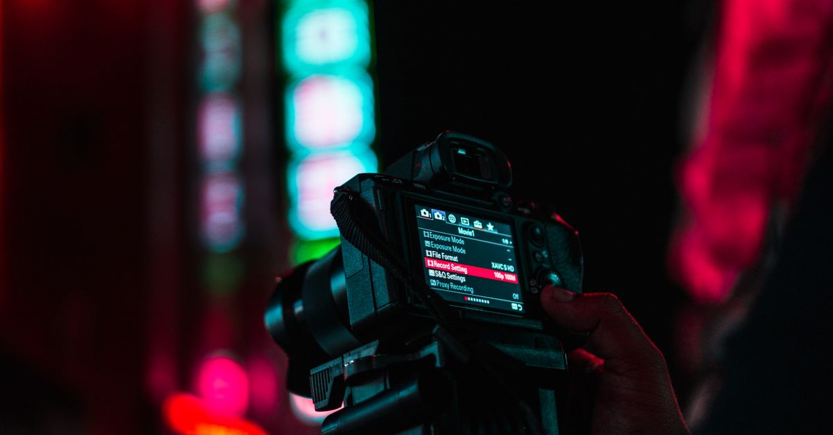 Close-up of a camera held in hand with vibrant neon lights. Nighttime urban photography.