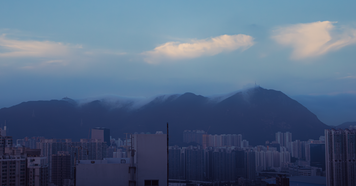 Explore the stunning Kowloon skyline during blue hour with a backdrop of scenic mountains and wispy clouds.