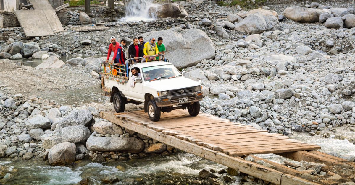 A truck full of adventurers crossing a wooden bridge in Swat Valley, Pakistan, showcasing rugged travel.