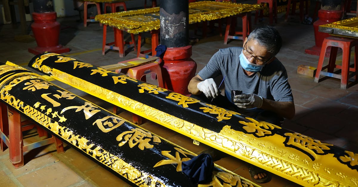 A skilled artisan intricately painting gold lettering on wooden panels in a workshop setting.