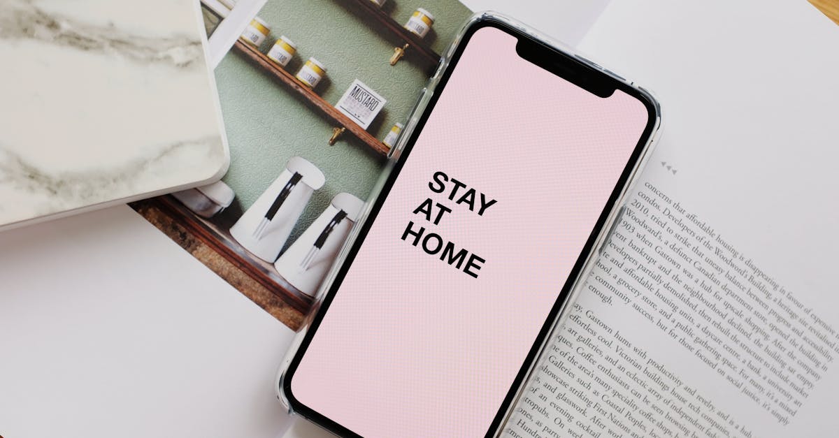 From above of modern cellphone with pale pink screen and STAY AT HOME inscription put on open magazine in apartment during COVID 19 pandemic