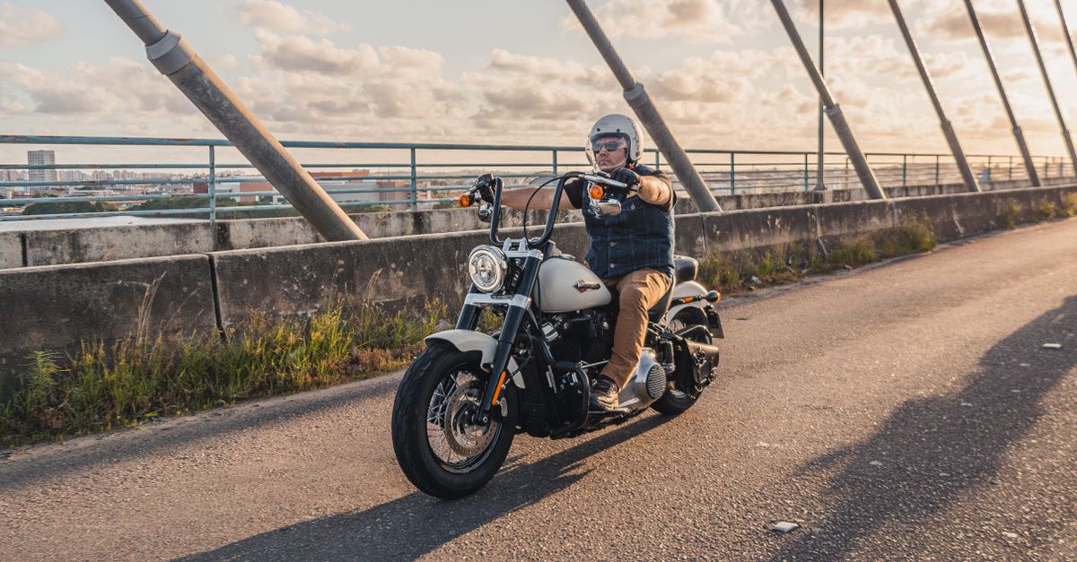 A motorcyclist on a cruiser bike cruises across a bridge at sunset.
