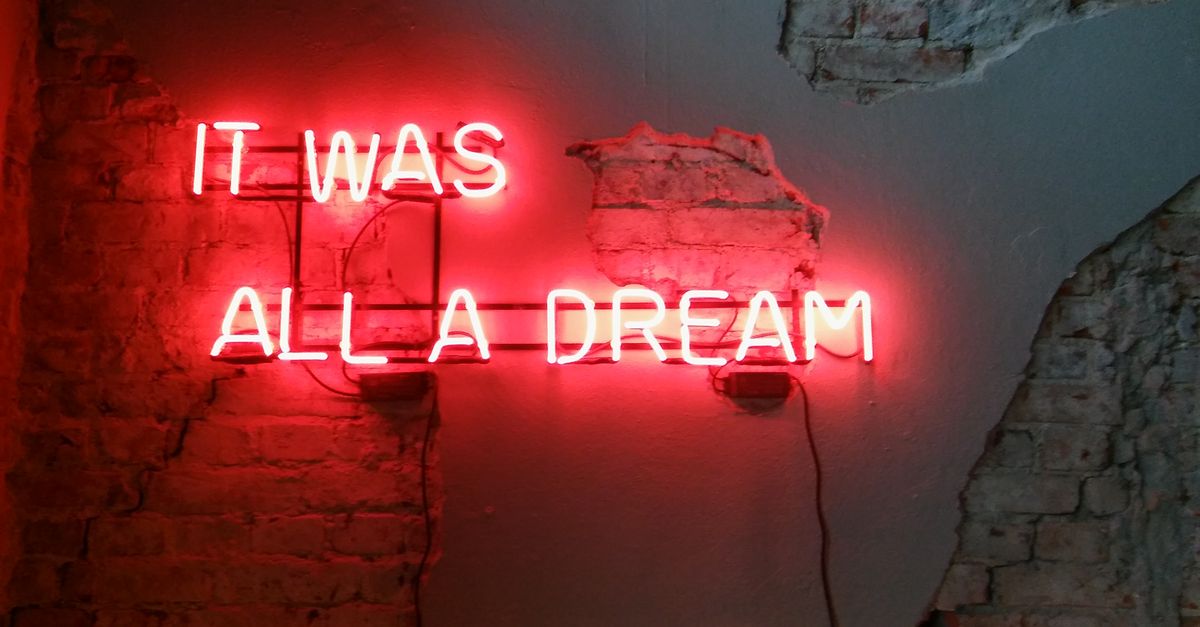 Vibrant neon sign reading "It Was All A Dream" on a textured brick wall in an urban setting.
