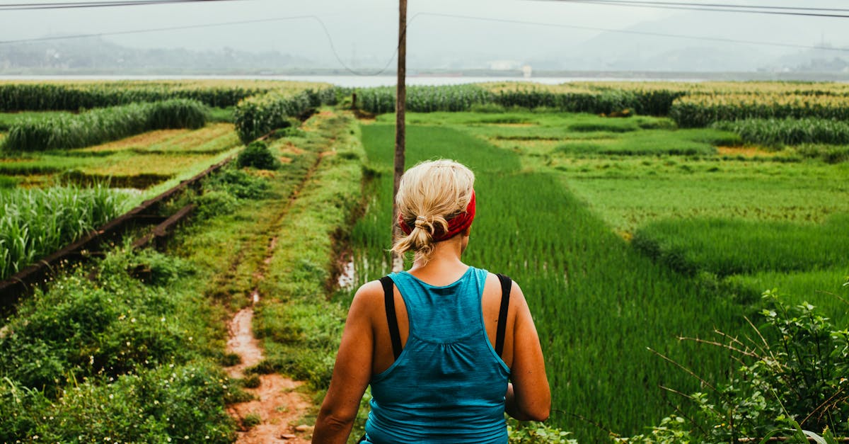 A woman enjoying a hike along a lush countryside path amidst green fields.