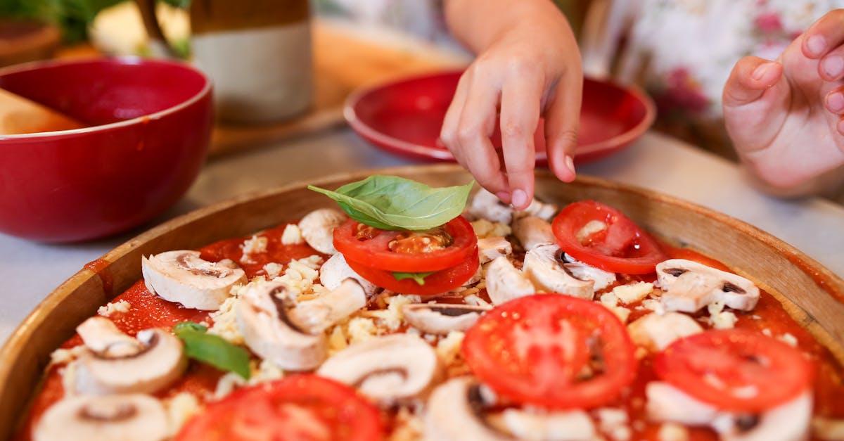 A child preparing a homemade pizza with fresh ingredients in the kitchen.