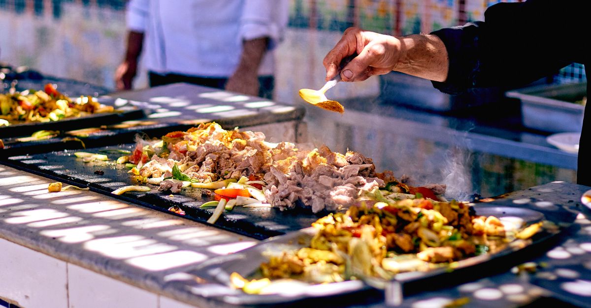 Chef adds spices to sizzling meat and vegetables at a vibrant street food stall.