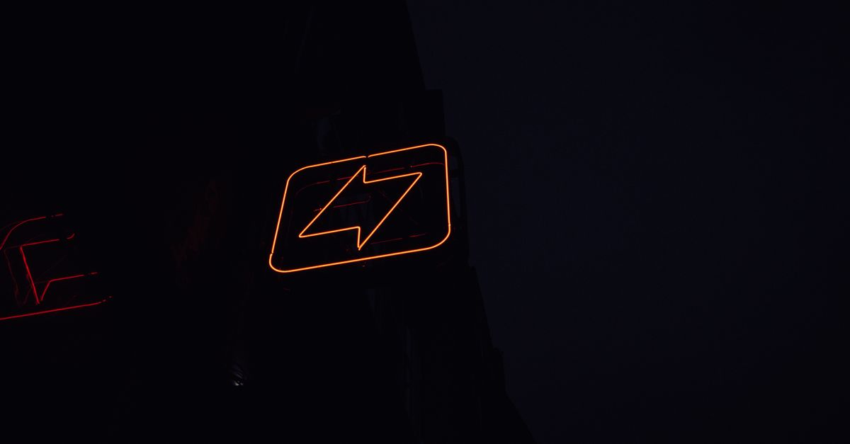A glowing neon lightning bolt sign against a dark night background, symbolizing energy and electricity.