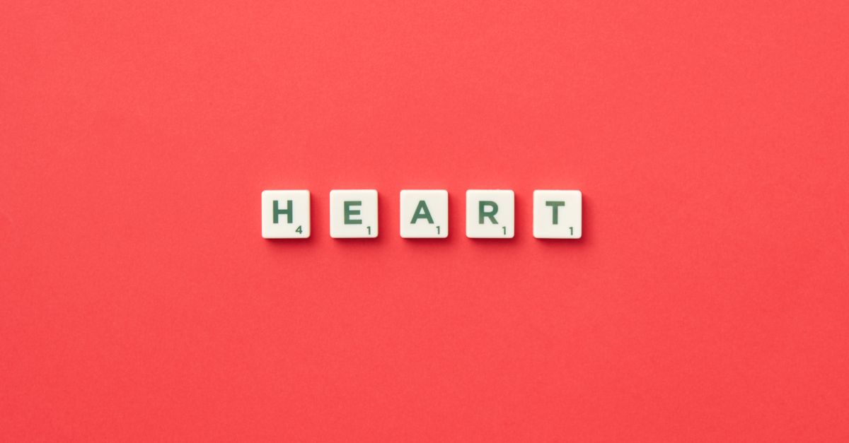 Top view of scrabble tiles spelling 'HEART' on a vibrant red background, perfect for love and games themes.