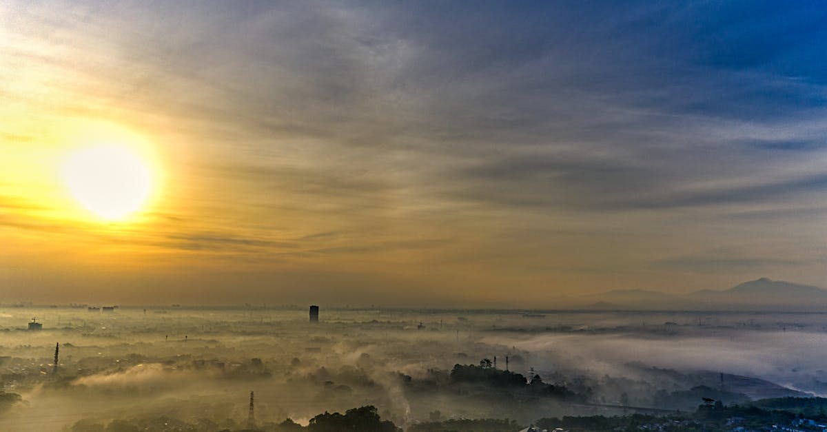 From above of picturesque scenery of sunrise sky with clouds over city covered with mist