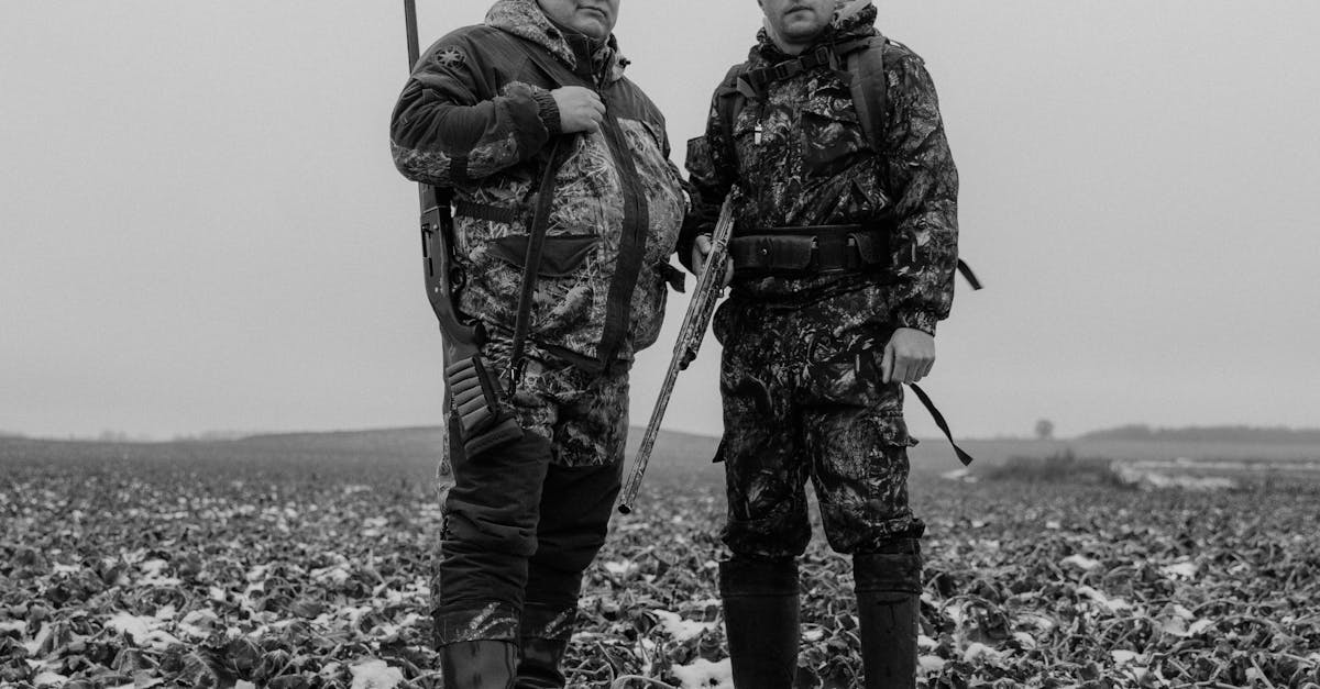 Two men in camouflage stand in a snowy field, ready for hunting.
