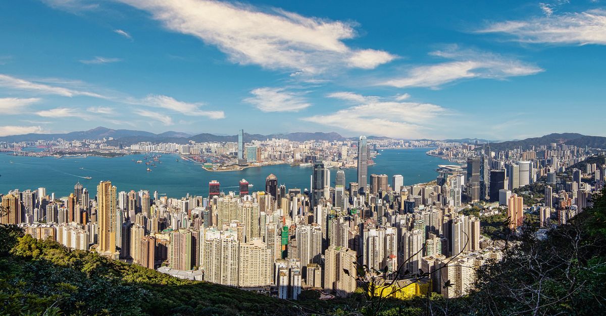 Stunning aerial view of Hong Kong's skyline with skyscrapers and Victoria Harbour under a clear blue sky.