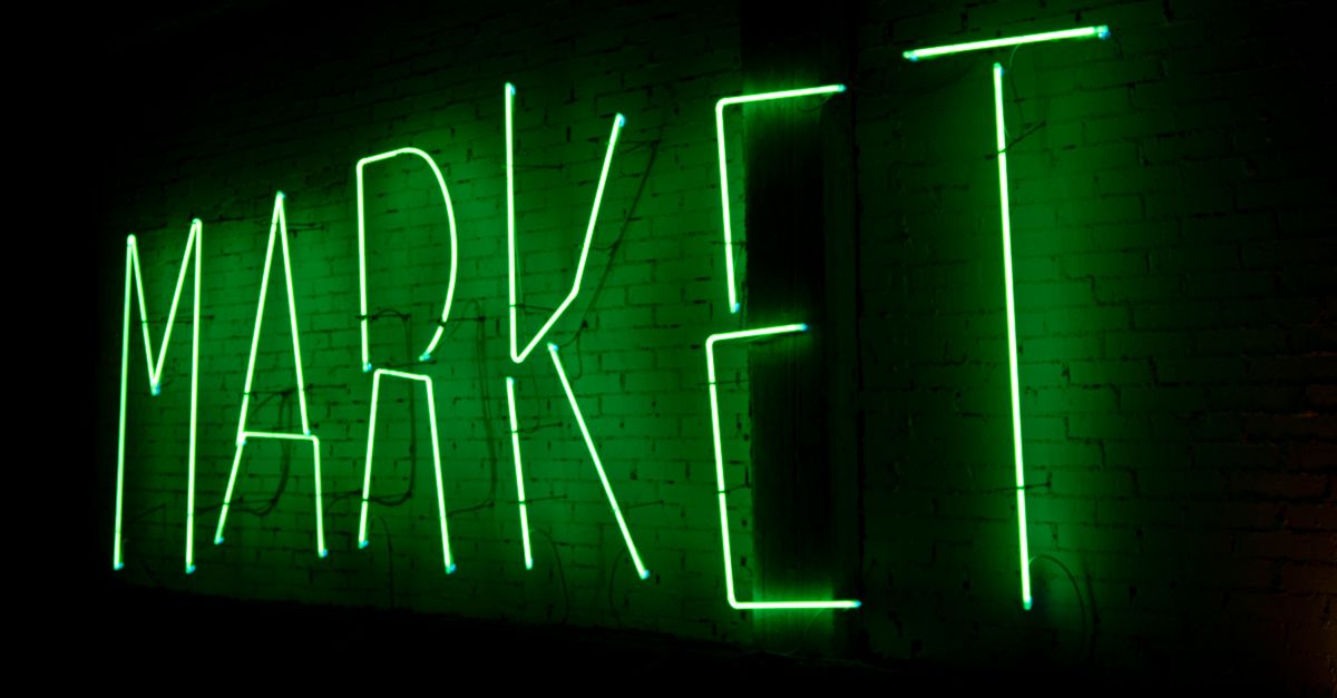 Vibrant green neon sign spelling 'MARKET' illuminating a brick wall at night.