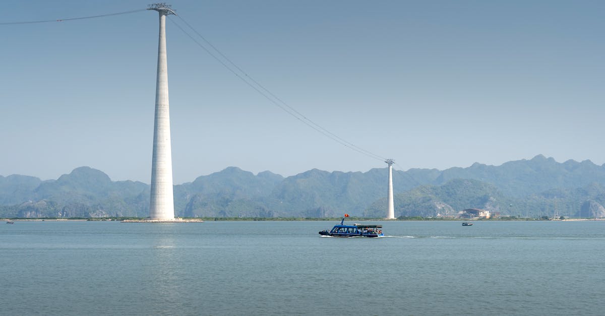 Scenic view of cable car tower over Halong Bay with a boat in foreground and hills in backdrop.