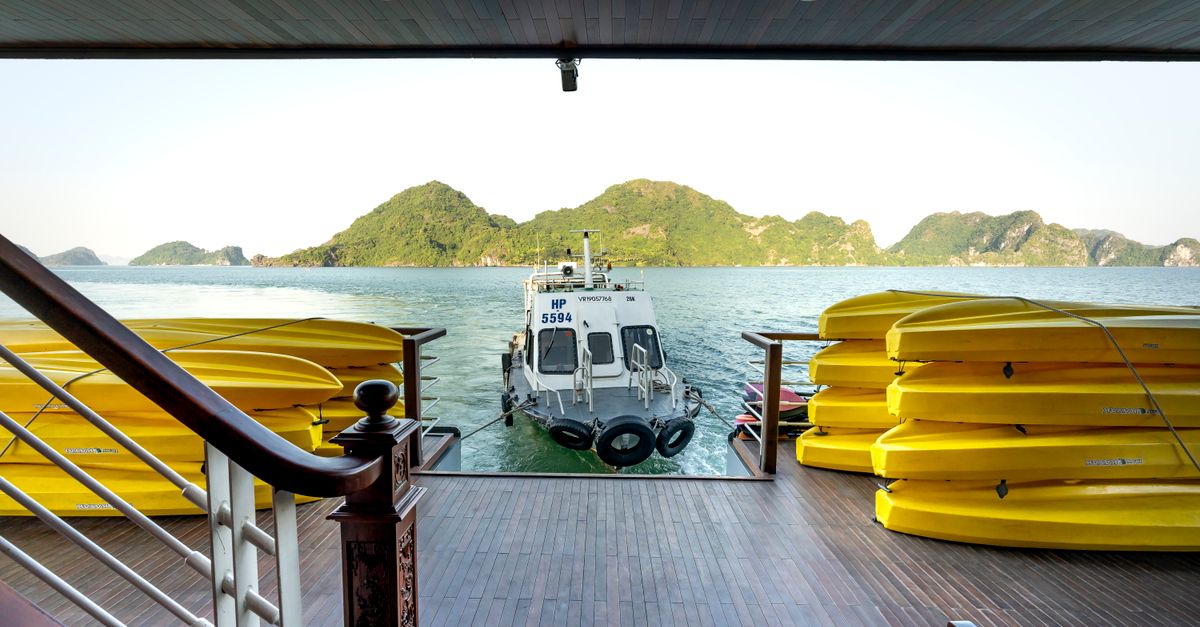A serene view of a boat docking at a tropical island surrounded by kayaks and lush hills.