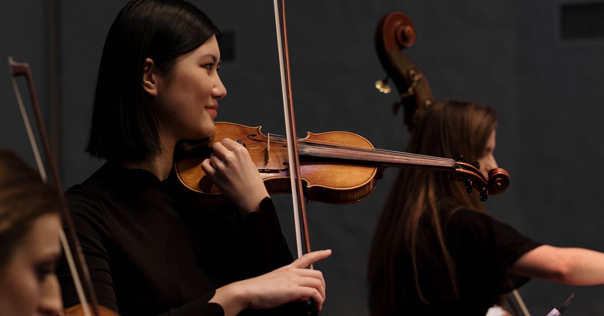 Asian female violinist performing on stage during a live concert.