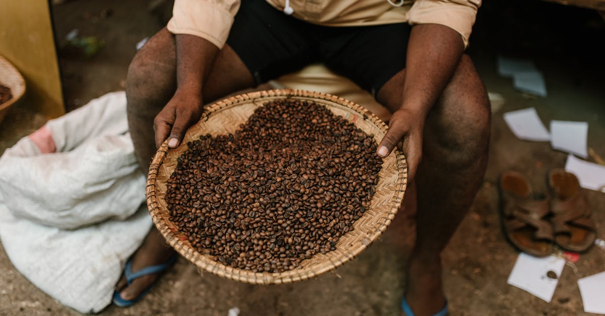 From above of unrecognizable ethnic person sitting with plate full of roasted coffee beans at local market