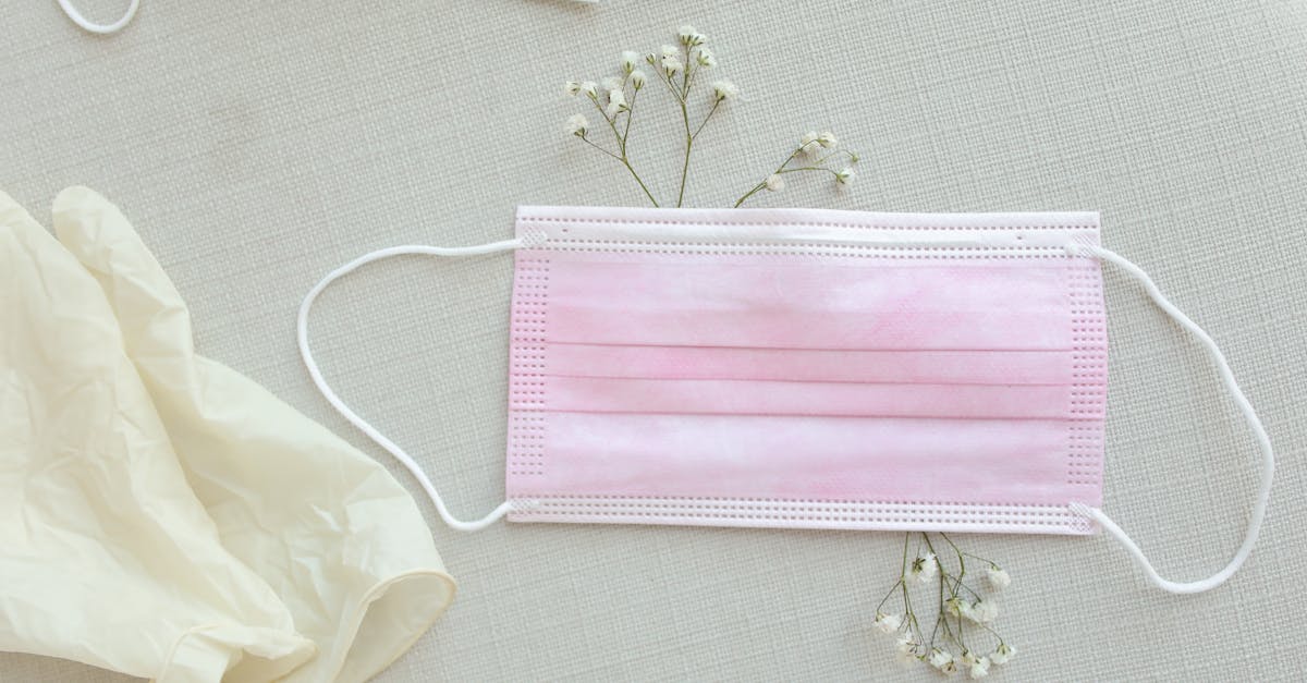 Pastel pink face mask with delicate flowers and a glove on a light textile surface.