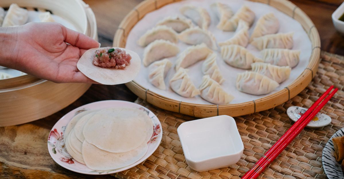 From above of crop anonymous female demonstrating dough circle with minced meat filling above table with dumplings at home