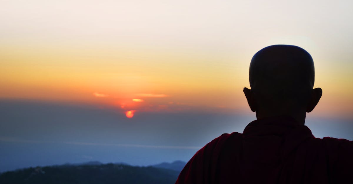Silhouette of a monk overlooking a serene sunset on a mountain in Myanmar, capturing tranquility.