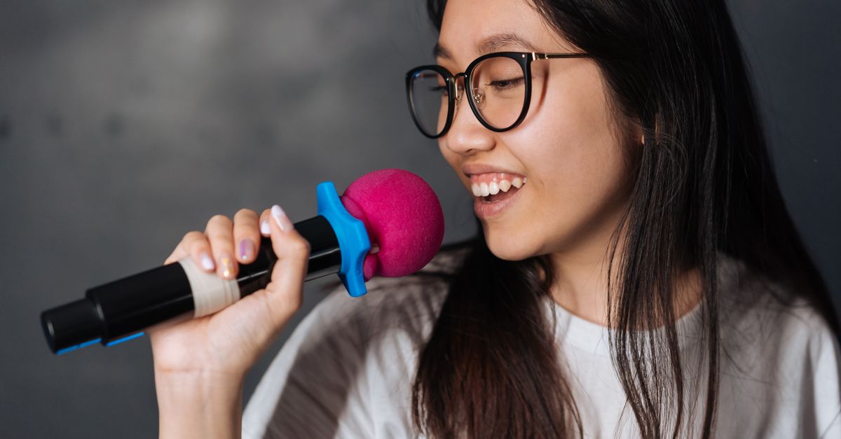 A young woman happily sings into a microphone during a karaoke session indoors.
