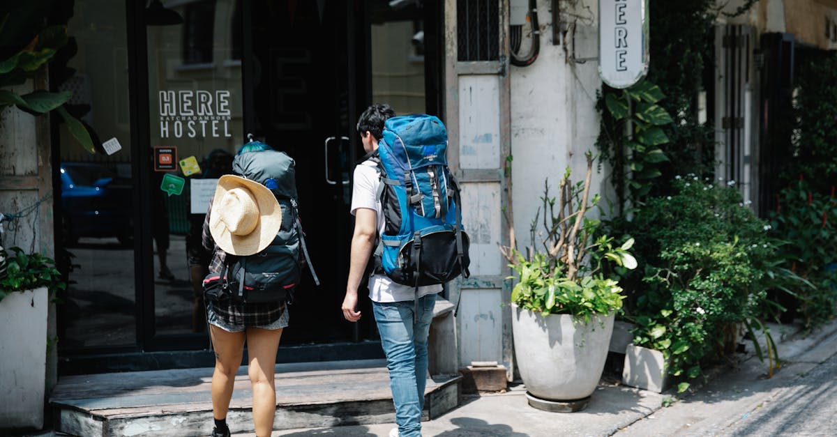Back view of anonymous couple of tourists with rucksacks walking on street and entering hostel door during trip