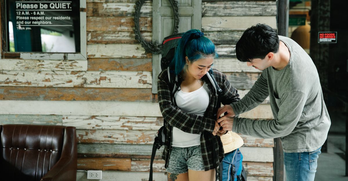 Two travelers prepare their backpacks in a rustic hostel lobby.