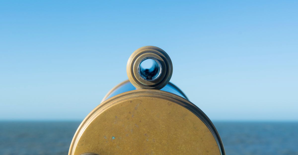 A close-up view through a brass telescope overlooking the ocean under a clear blue sky.
