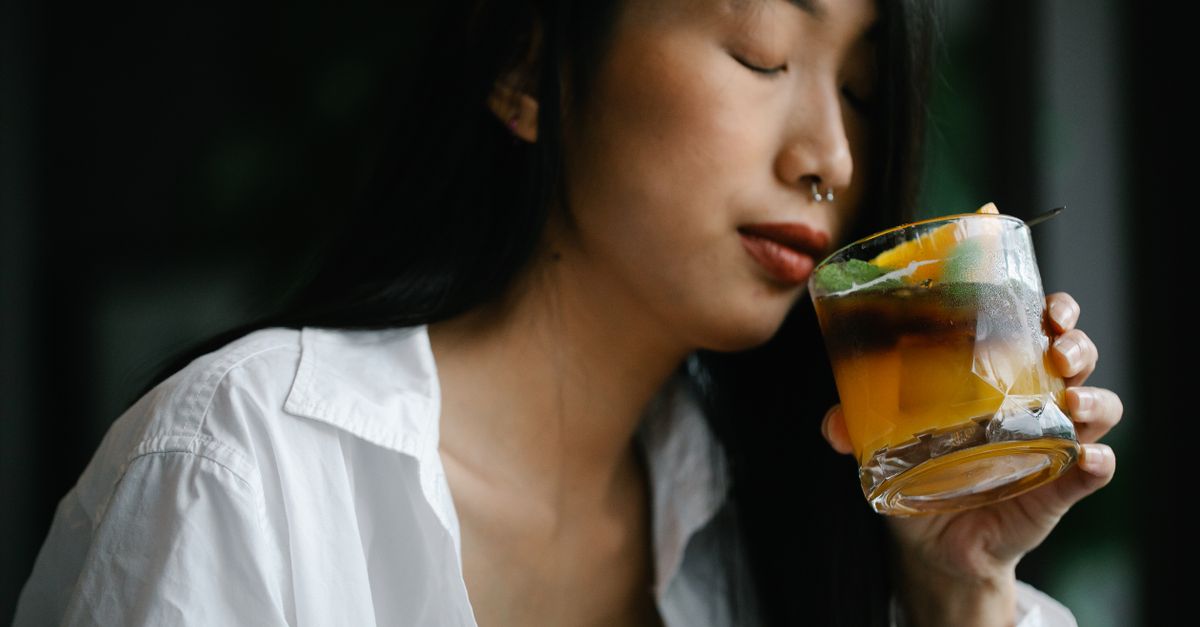 Woman savoring a cold cocktail with a mix of citrus and herbs, inside a cozy setting.