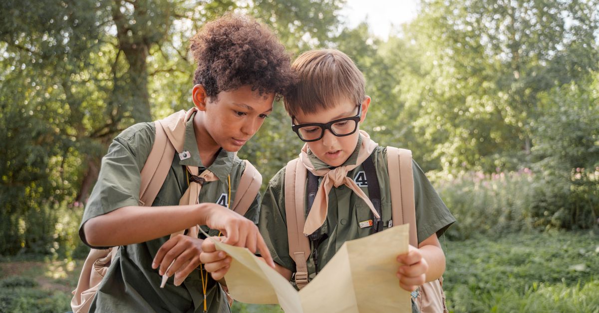 Two boys in scouting gear examine a map during an outdoor adventure.