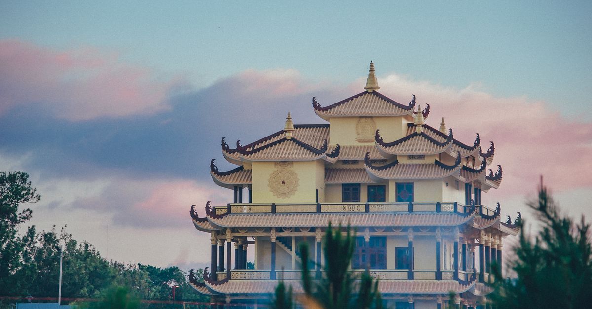A traditional Asian temple with ornate roof design at sunset amid lush greenery.