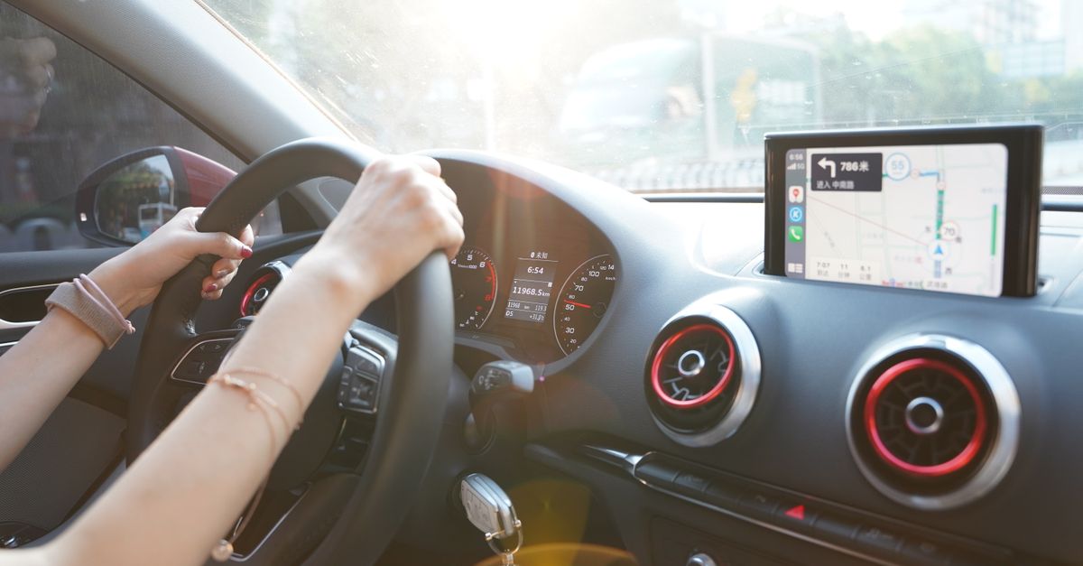 Hands on steering wheel using GPS navigation inside car during road trip.