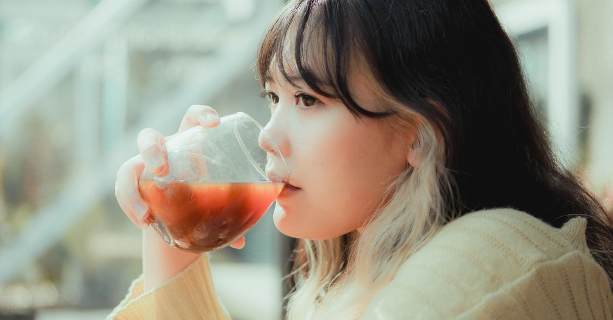 Side view of a woman sipping a refreshing drink indoors on a sunny day.