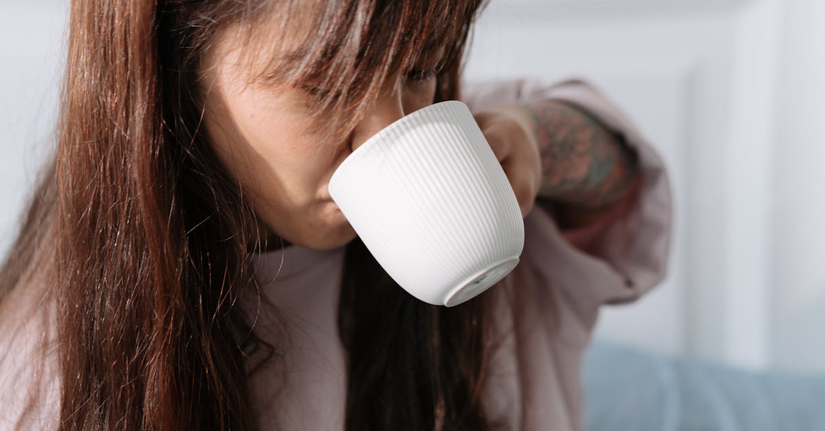 A woman with long hair sipping coffee from a white cup inside a cozy room.