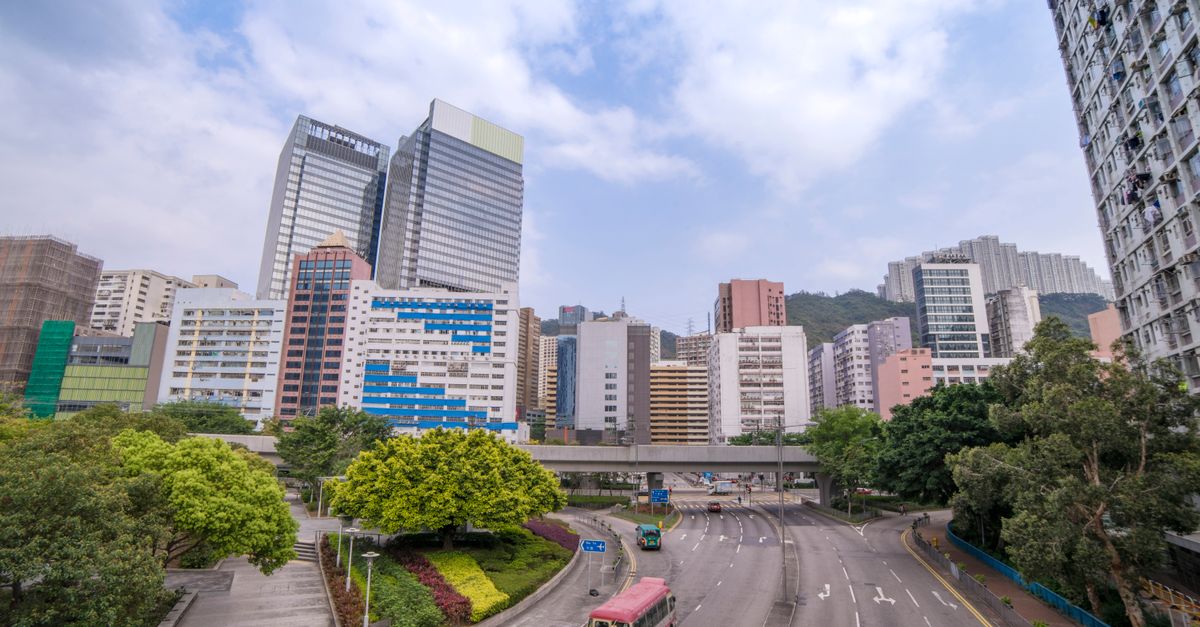 Wide-angle view of a Hong Kong cityscape featuring skyscrapers, greenery, and a vibrant road.